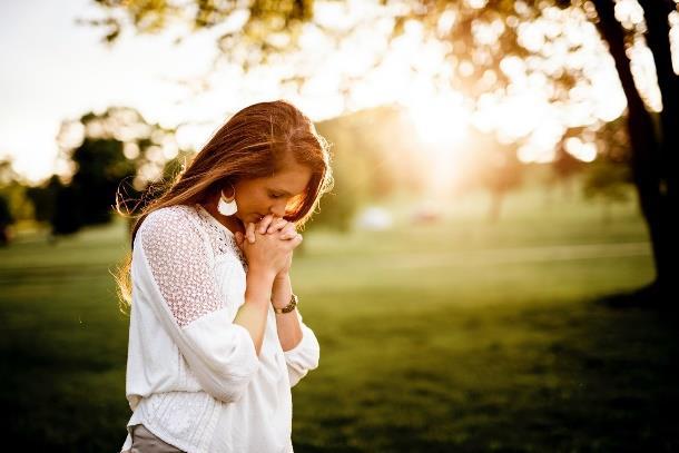 Young Christian woman praying outdoors in faith, seeking God's guidance through prayer and devotion.